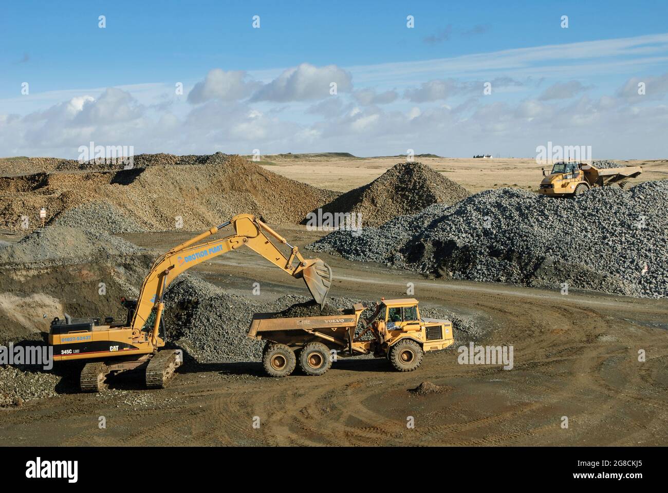 Caterpillar 345C excavator loading rocks into a Volvo articulated dump truck in a quarry in England. Stock Photo
