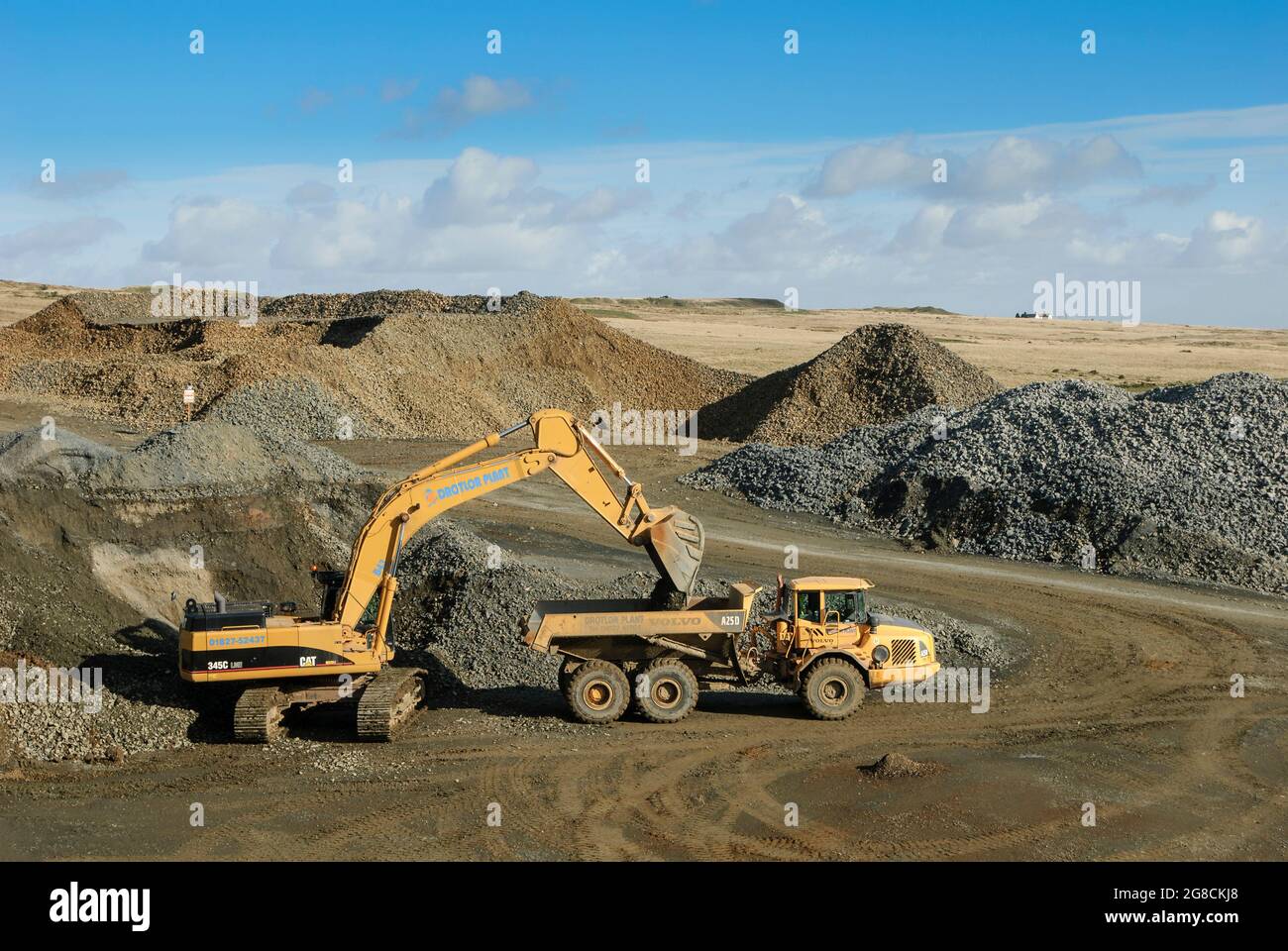 Caterpillar 345C excavator loading rocks into a Volvo articulated dump truck in a quarry in England. Stock Photo