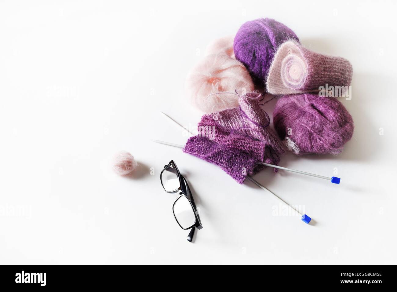 Knitting threads, knitting needles and glasses on white table background. Stock Photo