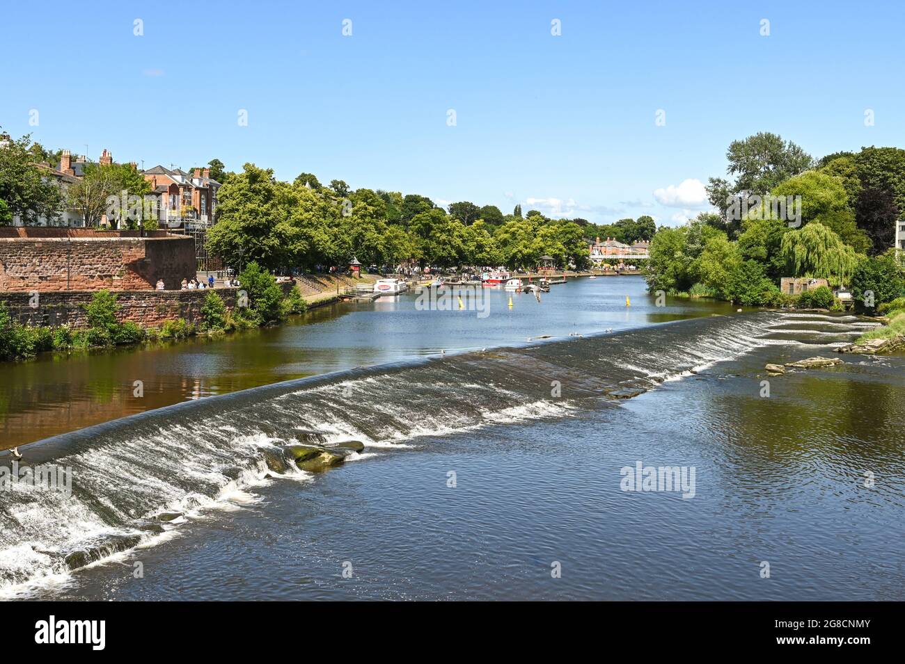 Chester, England - July 2021: Scenic view of boats on the River Dee, which flows through the city. In the foreground is a weir and fish pass. Stock Photo