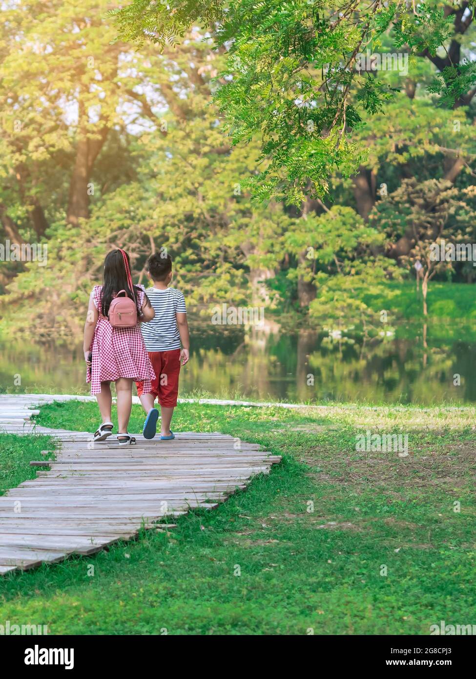 Back view of Asian young girl and boy walking together on pathway ...