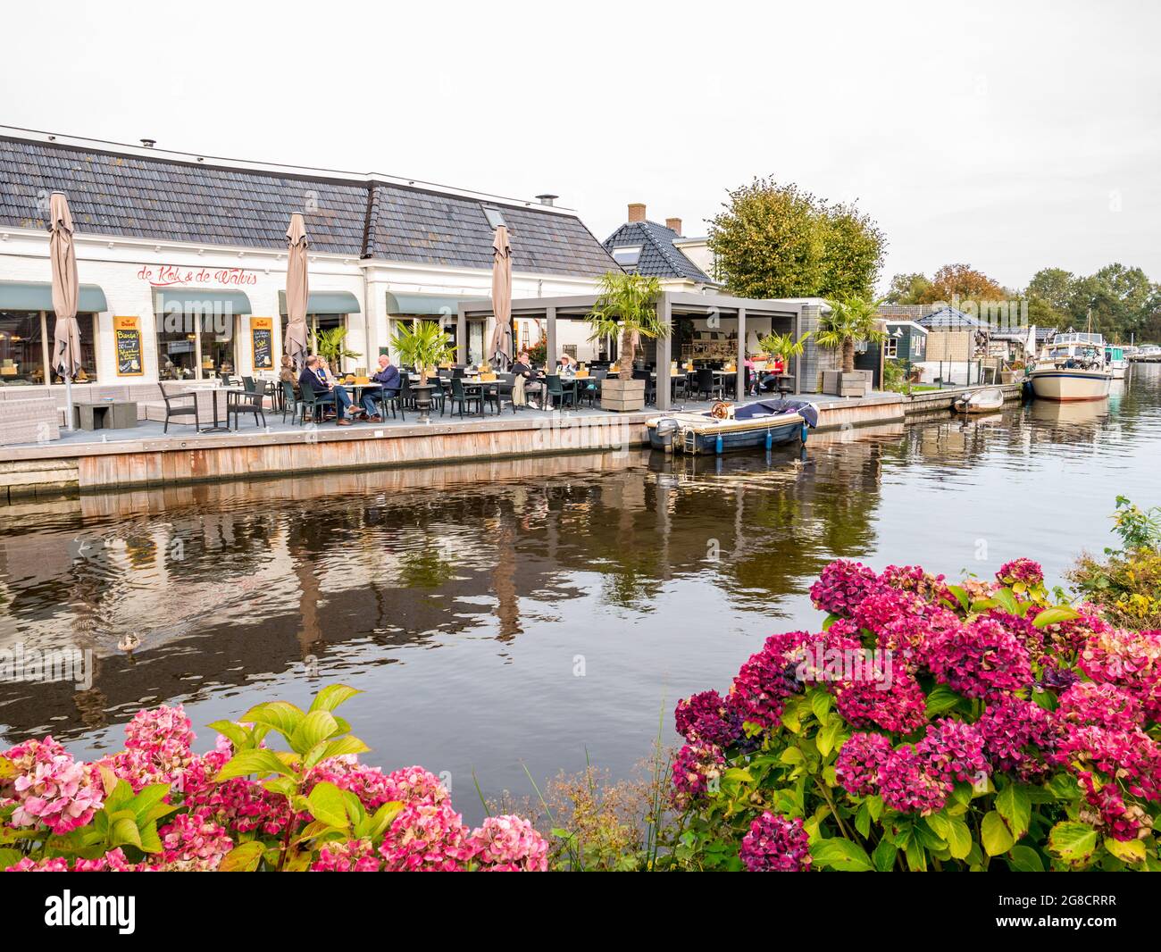People on outdoor terrace of cafe restaurant by canal in old village of Wartena, Leeuwarden, Netherlands Stock Photo