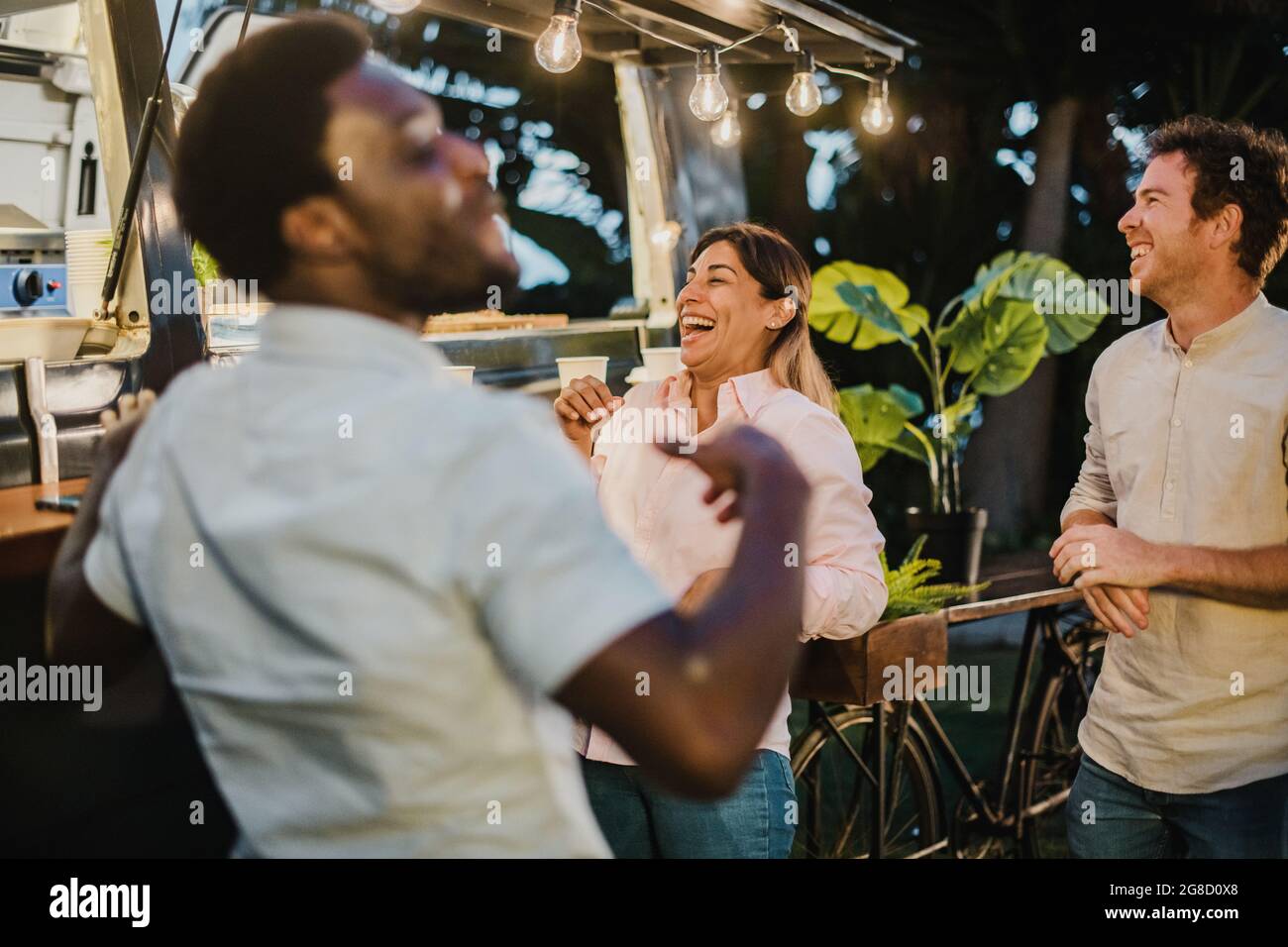 Diverse friends laughing outside food truck in evening Stock Photo