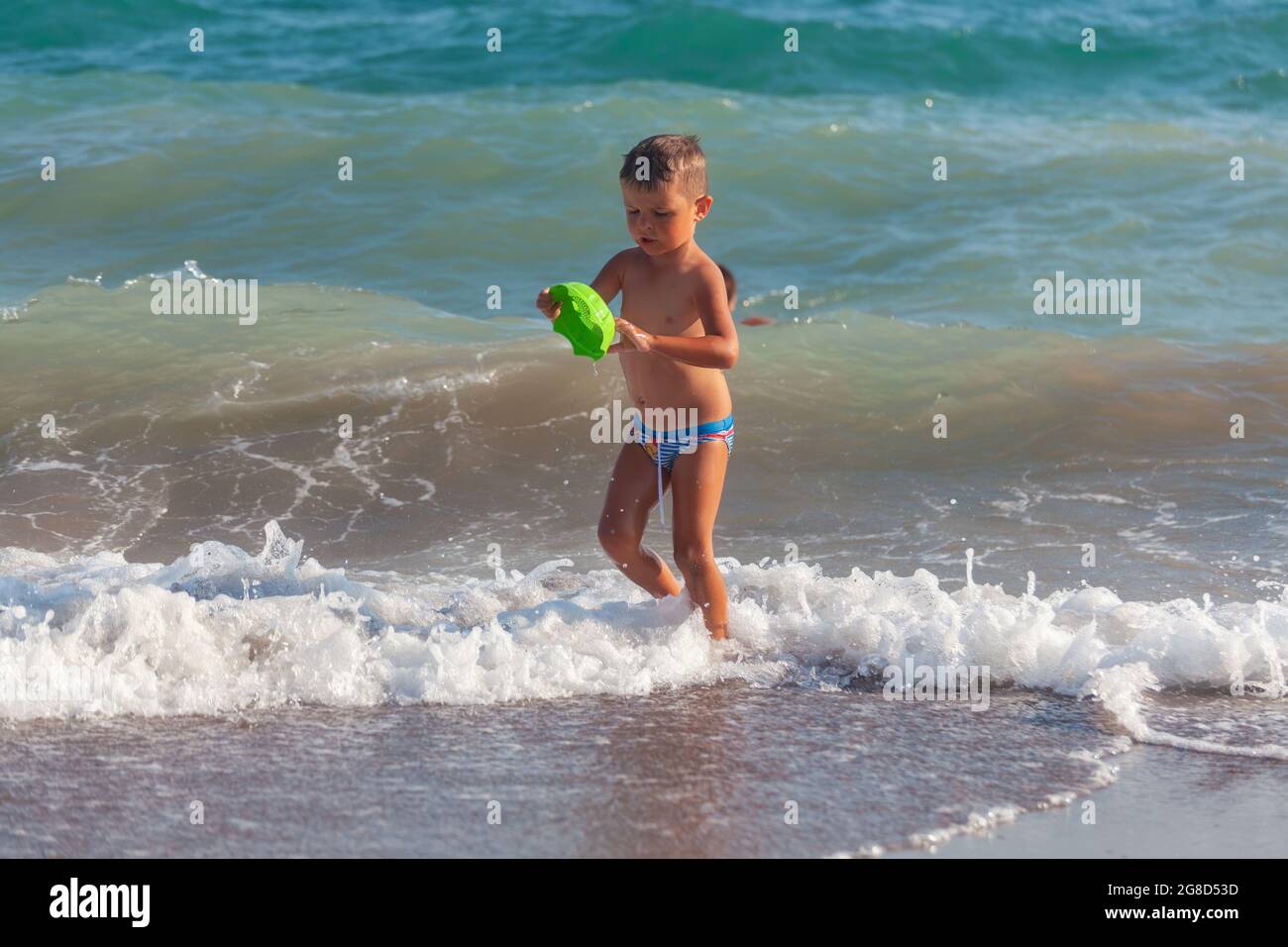 Antalya, Turkey-August 26, 2013: Cute little boy playing with plastic toy while walking on the seashore in a hot summer day in Antalya, Stock Photo