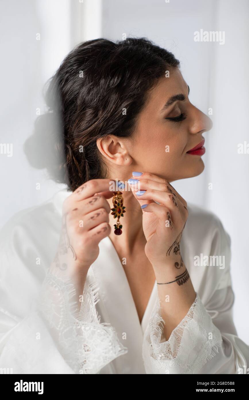 pretty indian bride wearing earring while getting ready for wedding on white Stock Photo