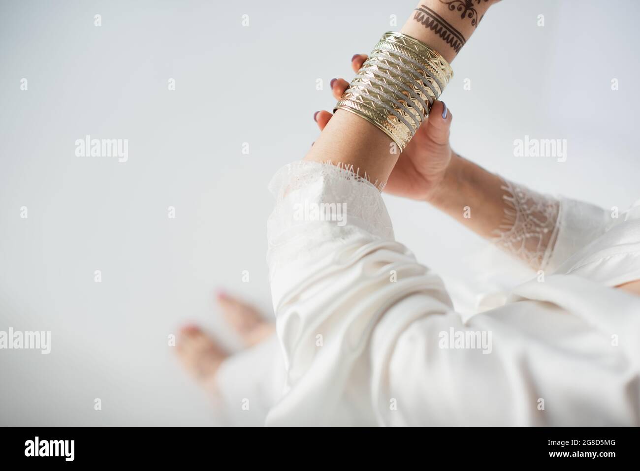 partial view of indian woman with mehndi on hands wearing golden bracelet while getting ready to wedding on white Stock Photo