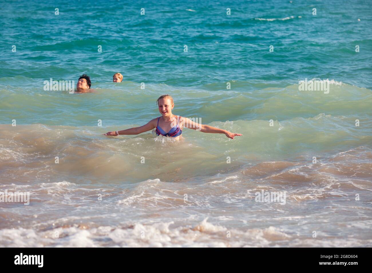 Antalya, Turkey-August 26, 2013: Joyful happy young girl and other people swimming  in wavy sea in summer in Antalya. Stock Photo