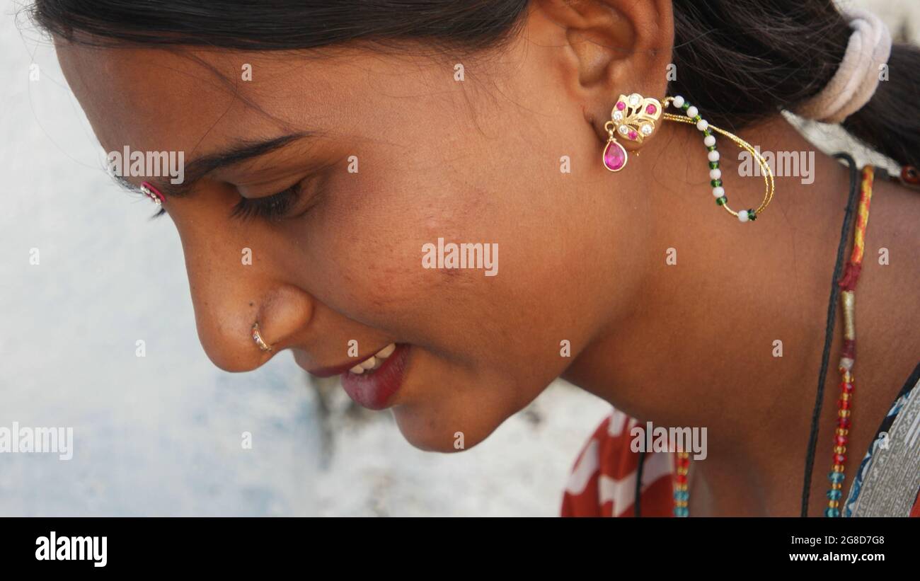 Portrait of a young Indian female with earrings and a nose piercing looking down with a cute smile Stock Photo