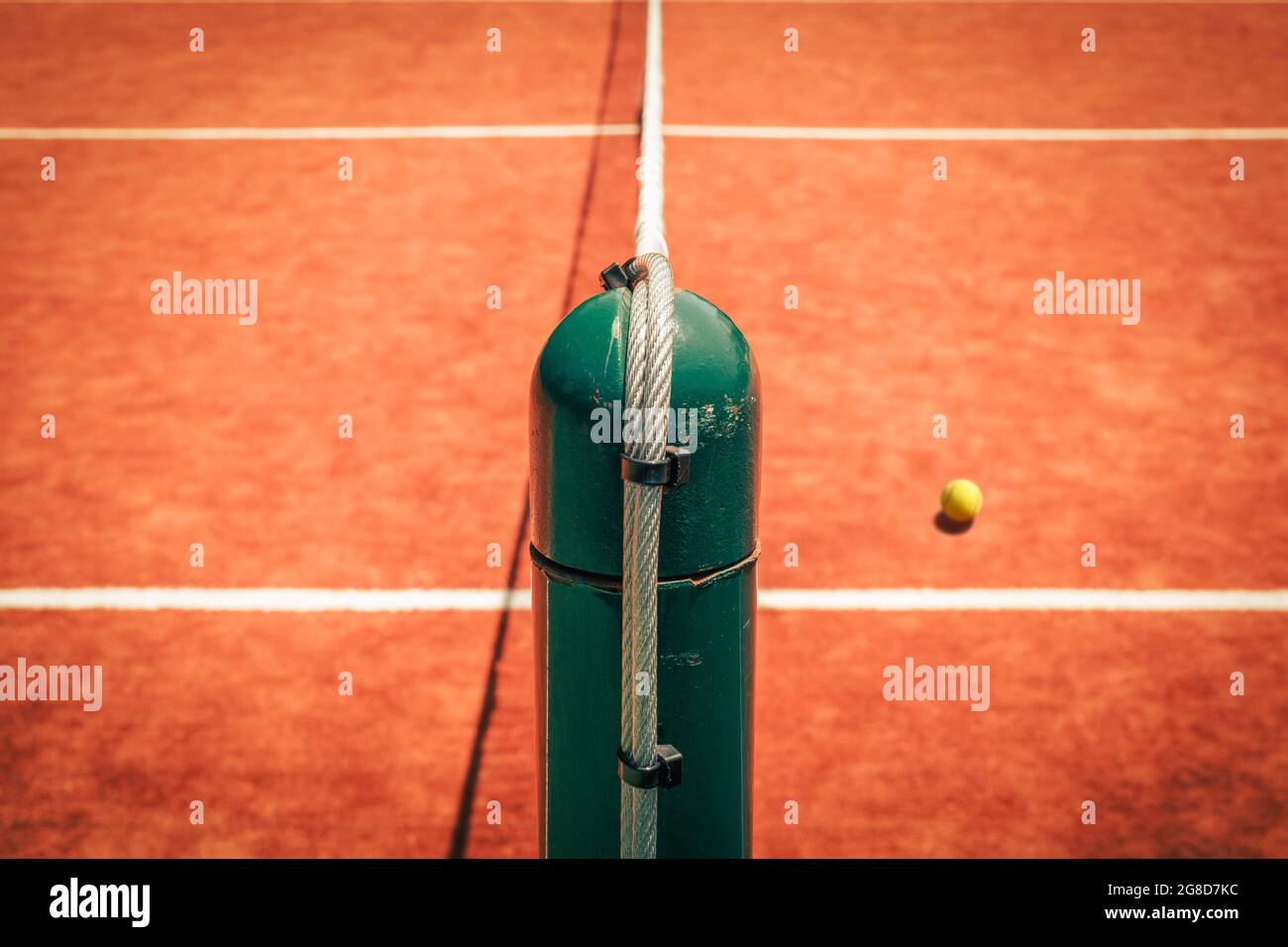 Worn steel tennis post and tennis ball from high angle. Tennis post dividing court to halves. Competitive individual sports concept. Stock Photo