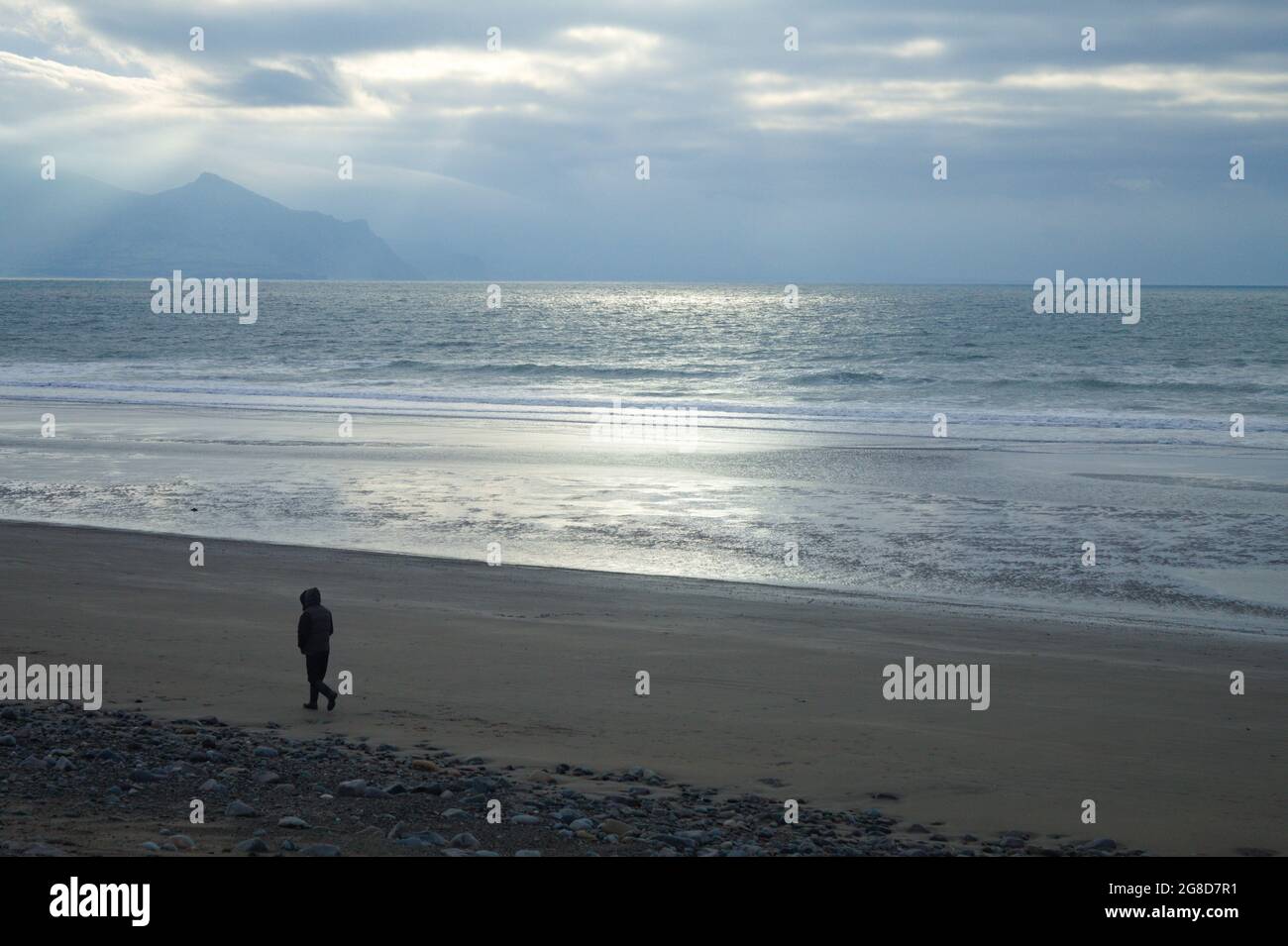 Dinas Dinlle beach, Caernarfon, north Wales. Winter landscape with an atmospheric view of the coast and sea. A solitary person walks on the sands. Stock Photo