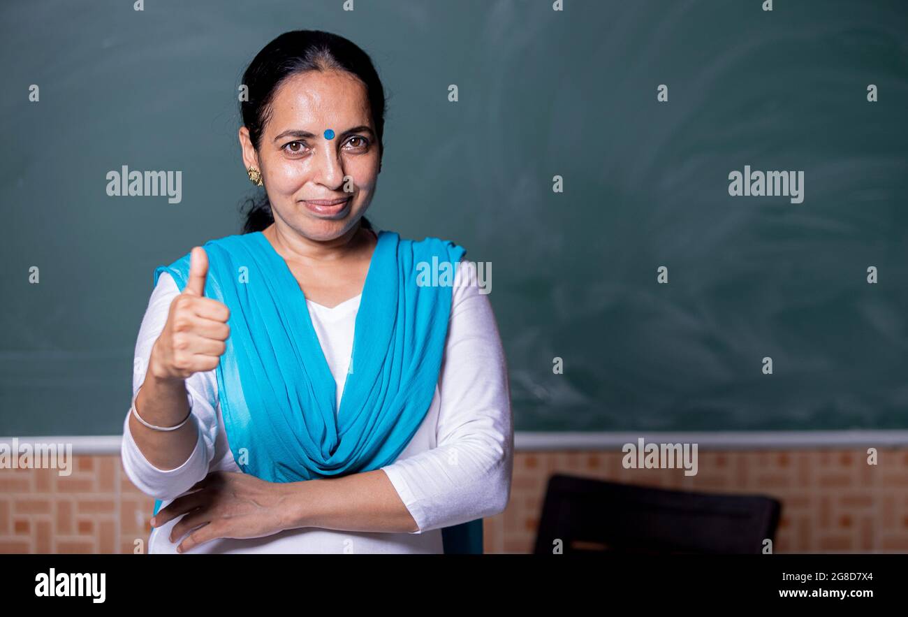 portrait of confident Indian teacher standing in front of the black ...