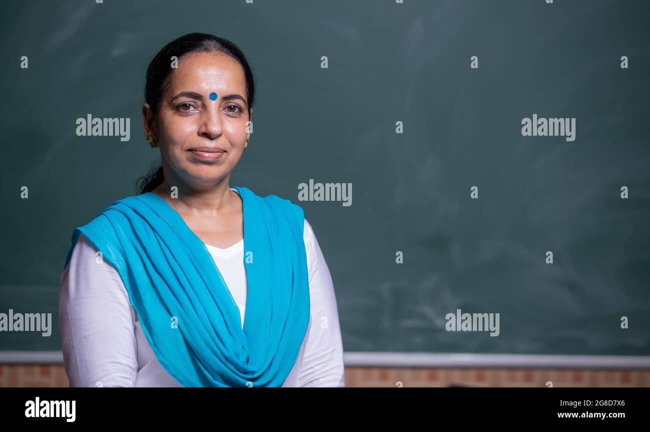 portrait of confident Indian teacher standing in front of the black ...
