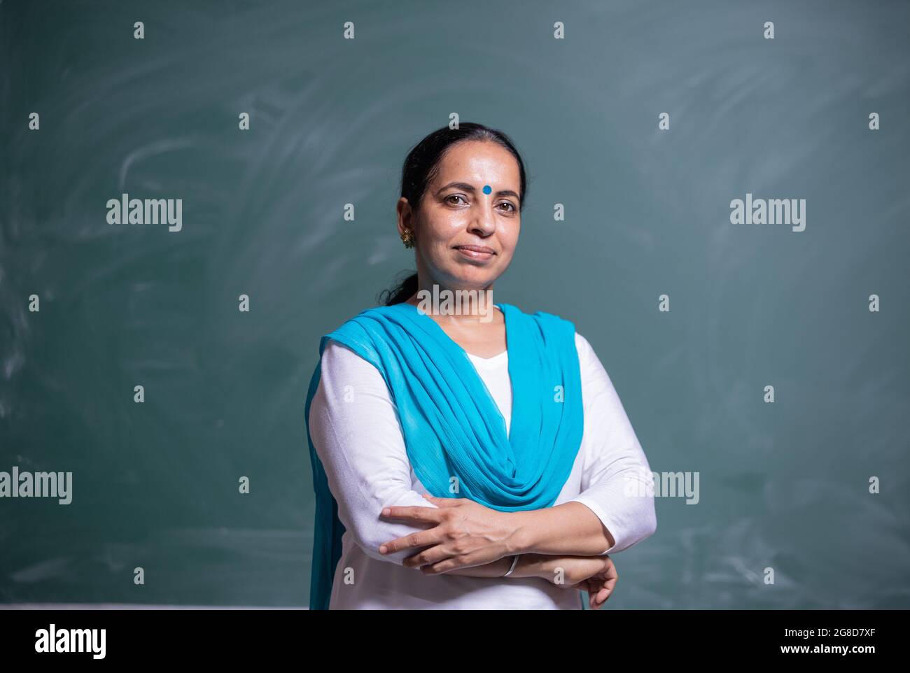 portrait of confident Indian teacher standing in front of the black ...