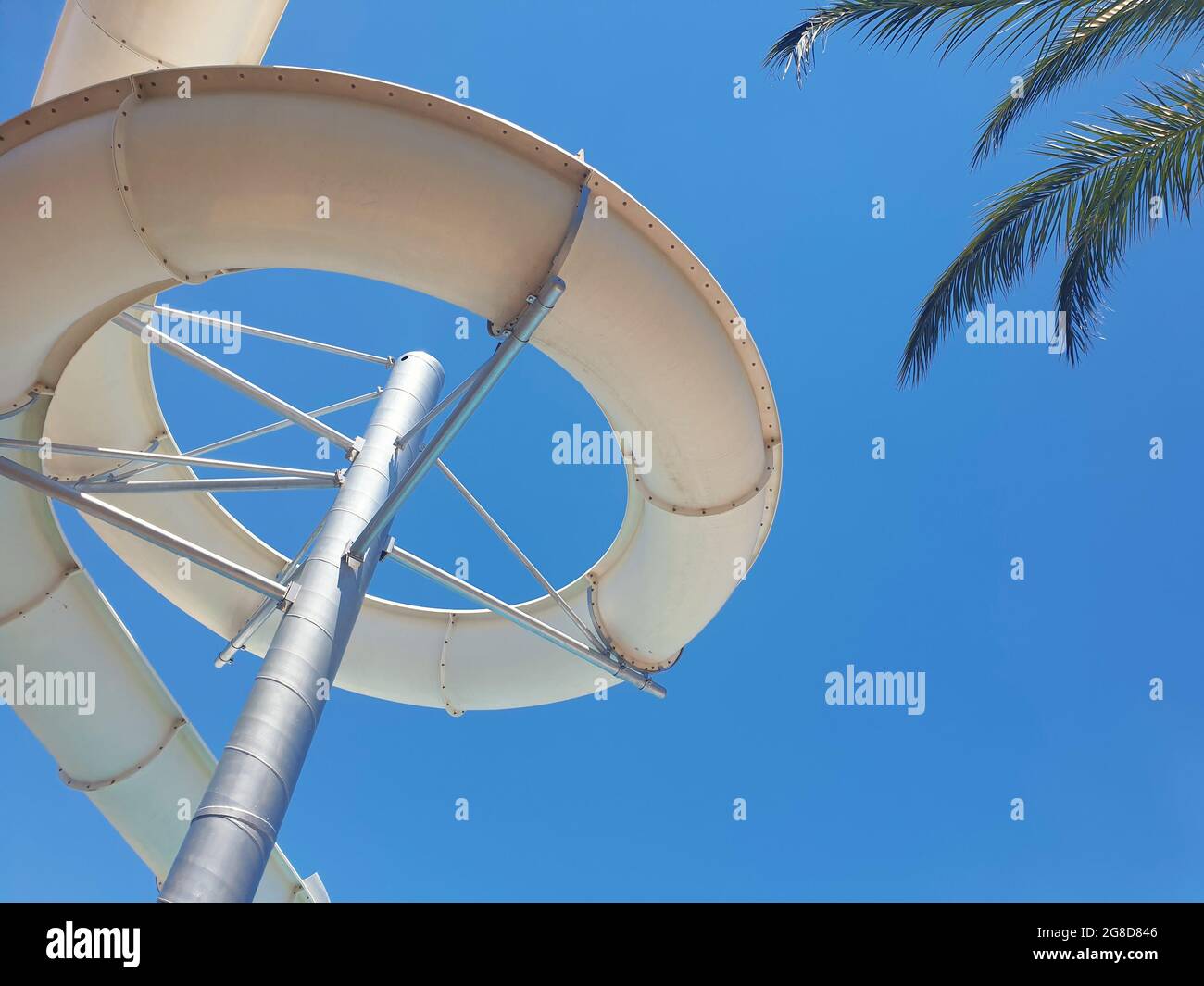 Screw water slide and palm tree leaves from below at water park summer holiday.  Summertime background with copy space. Stock Photo