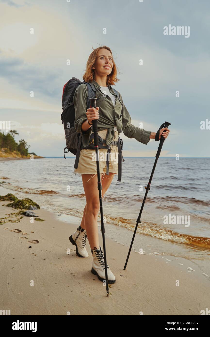Optimistic traveller using walking poles during beach stroll Stock Photo