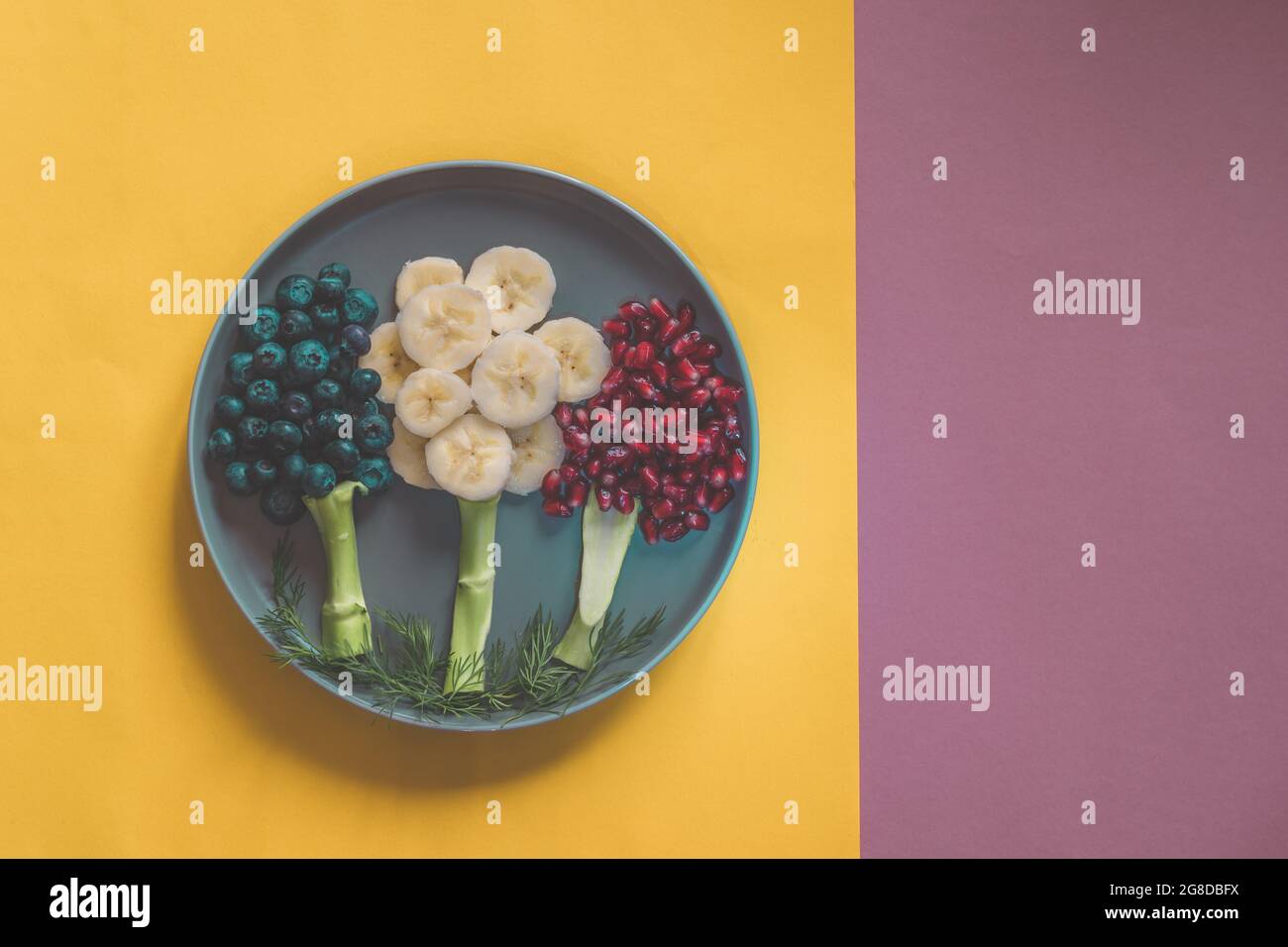 fruit trees on the plate made from banana, blueberries, pomegranate apples isolated on pink and yellow backgrounds Stock Photo