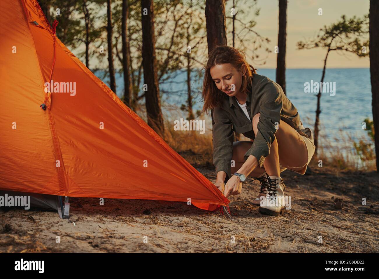 Lively woman installing an orange tent in the woods Stock Photo