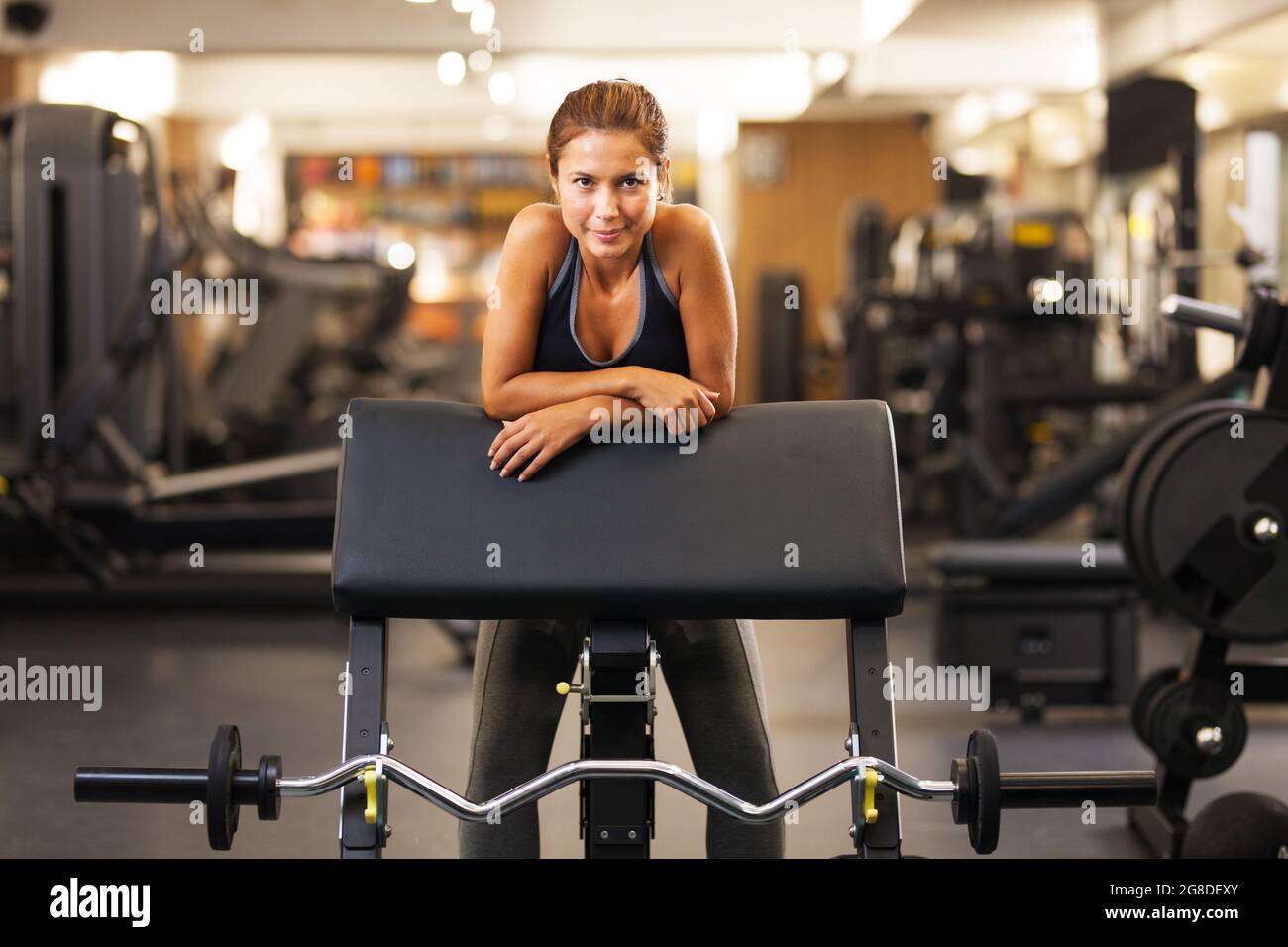 happy girl posing on a weight lifting seat in a generic out of focus fitness club Stock Photo