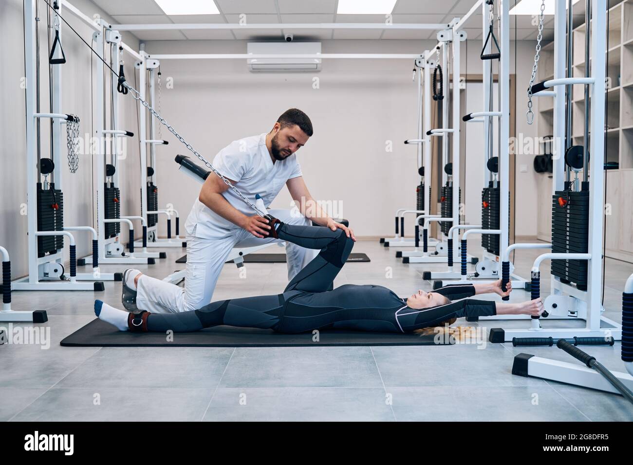 Young woman bending knee with attached rope of rehabilitation equipment