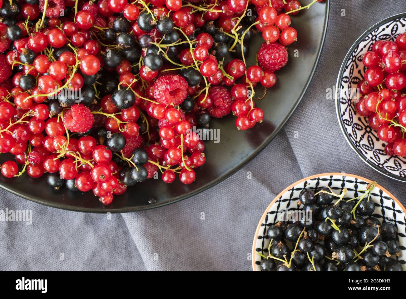 Bowl full of red and black currants and raspberries on a gray cloth ...