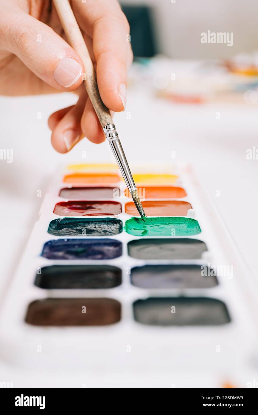 Close-up view of hand holding a brush and mixing the colors of paints on palette. Concept of art education, art class or studio and art therapy. Color Stock Photo