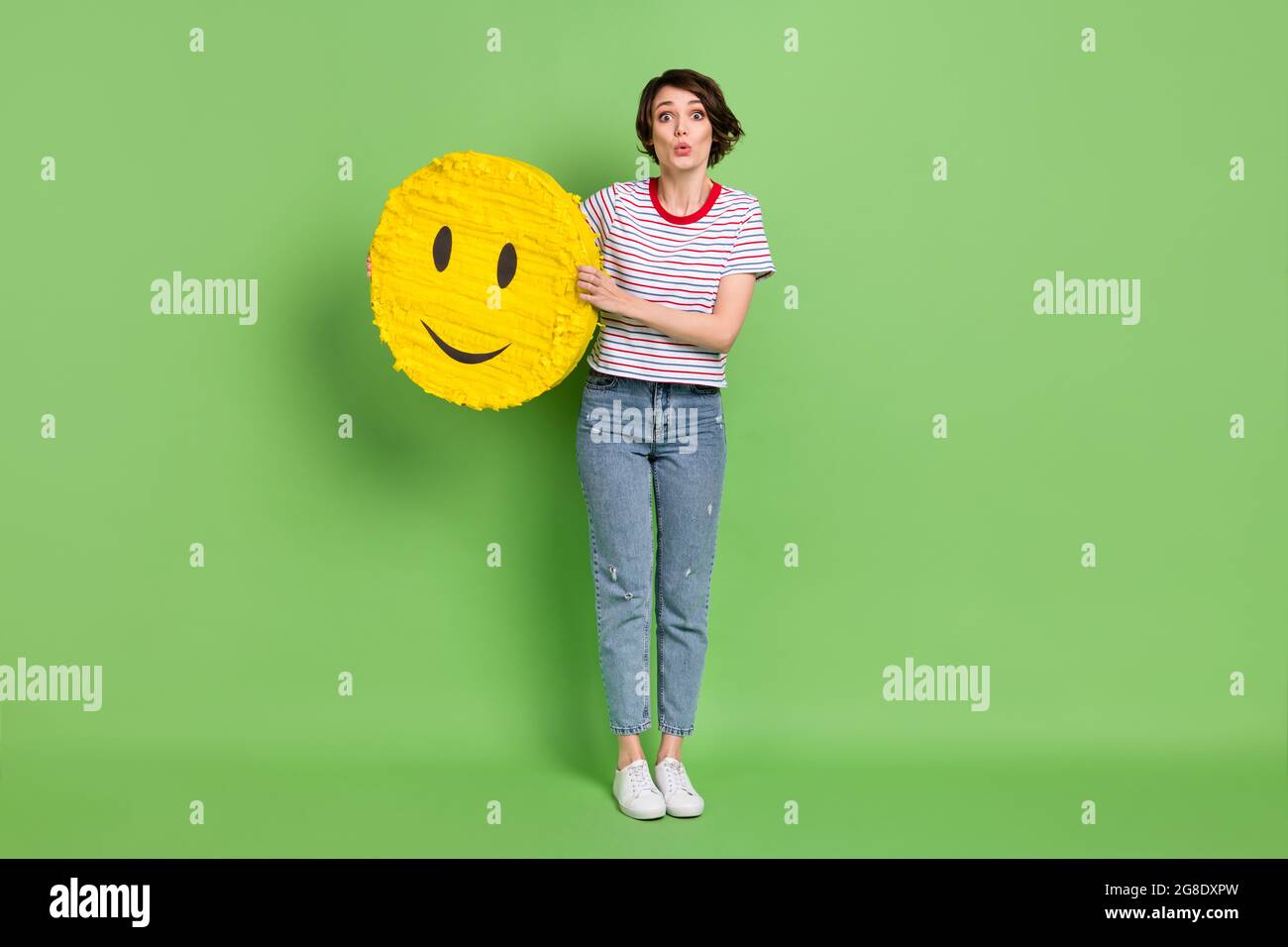 Full length body size view of pretty amazed girl holding in hands emoji sticker pout lips isolated over green pastel color background Stock Photo