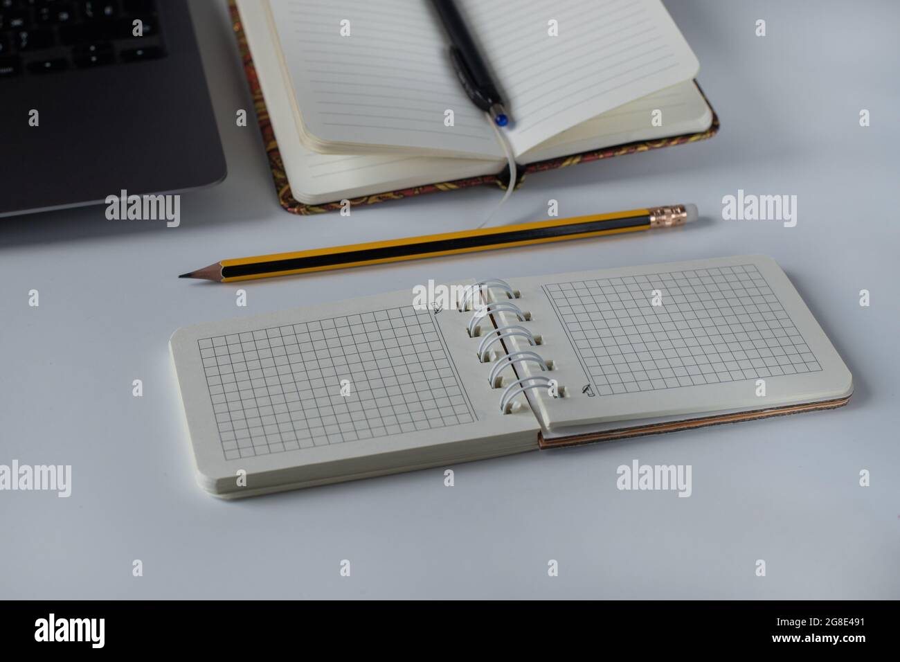 Office desk with spiral notepad, pencil and laptop on white background Stock Photo
