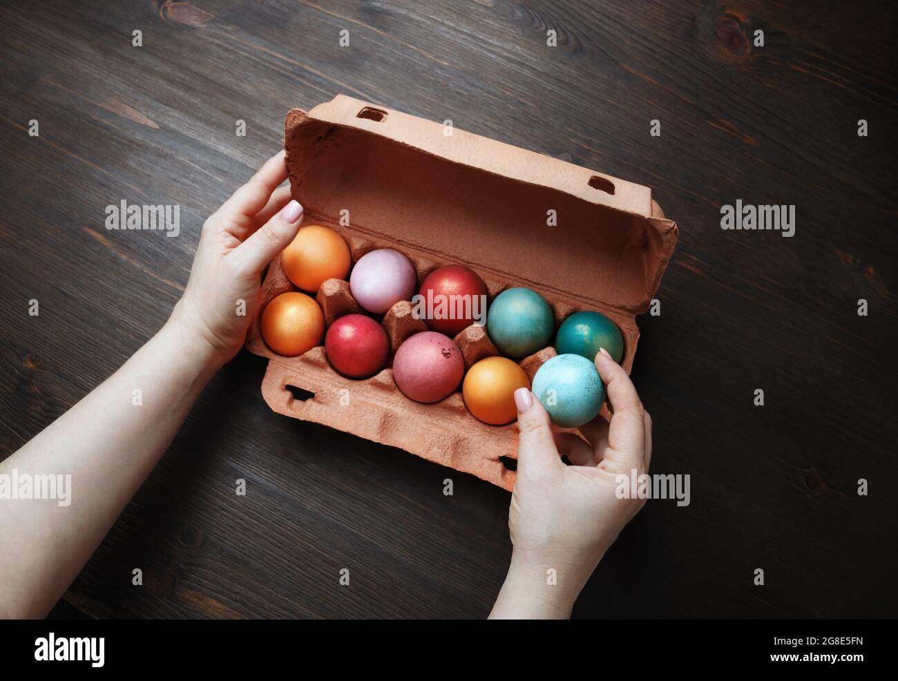 Colored Easter eggs in package and female hands on wood table background. Stock Photo