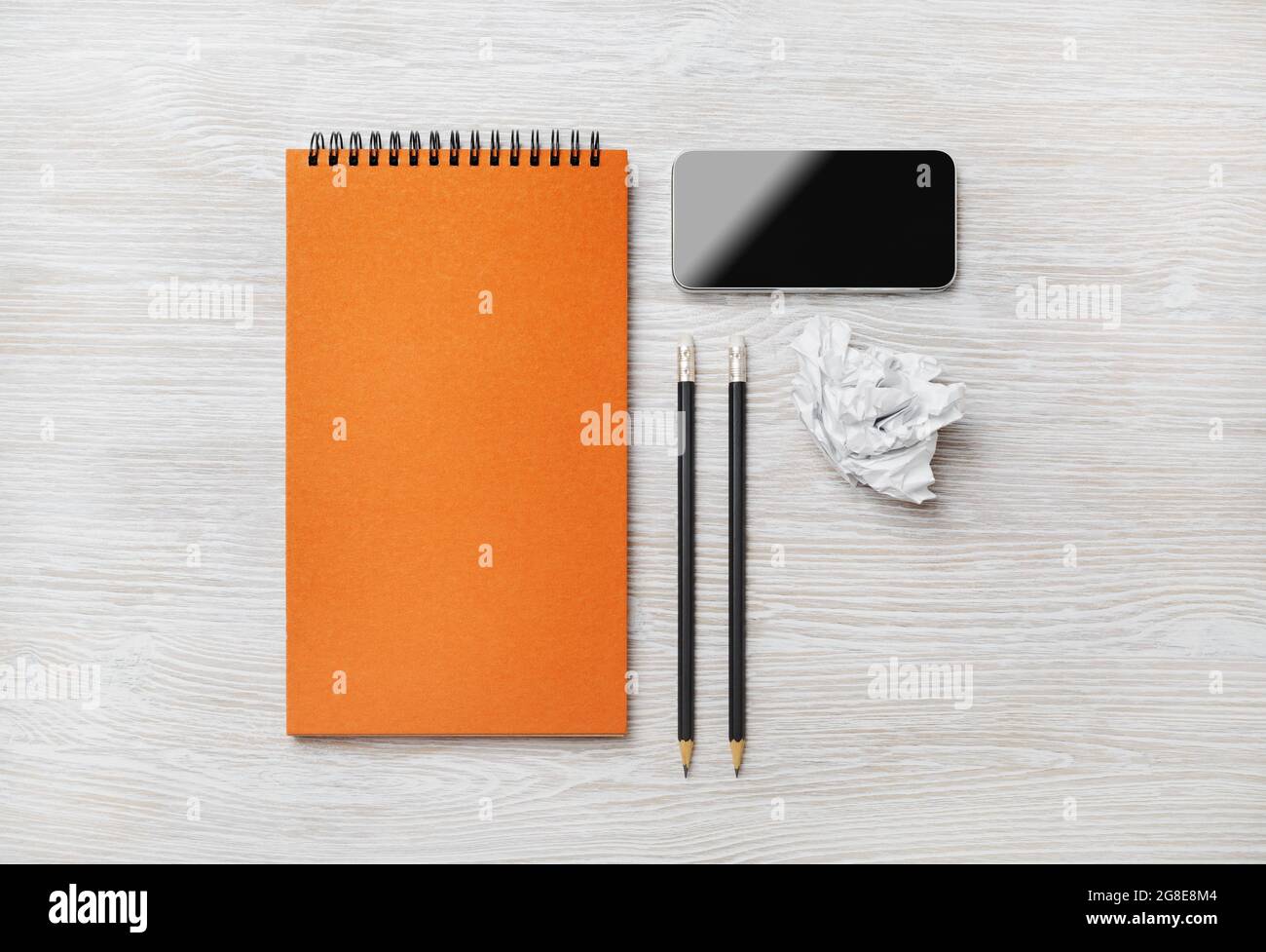 Blank orange notepad, smartphone, pencils and crumpled paper on light ...
