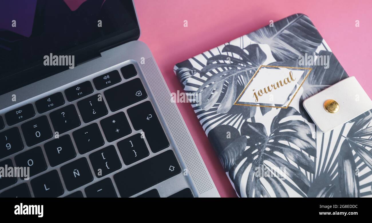 A laptop and a journal on pink background. Productivity and lifestyle concept. Handwriting. Stock Photo