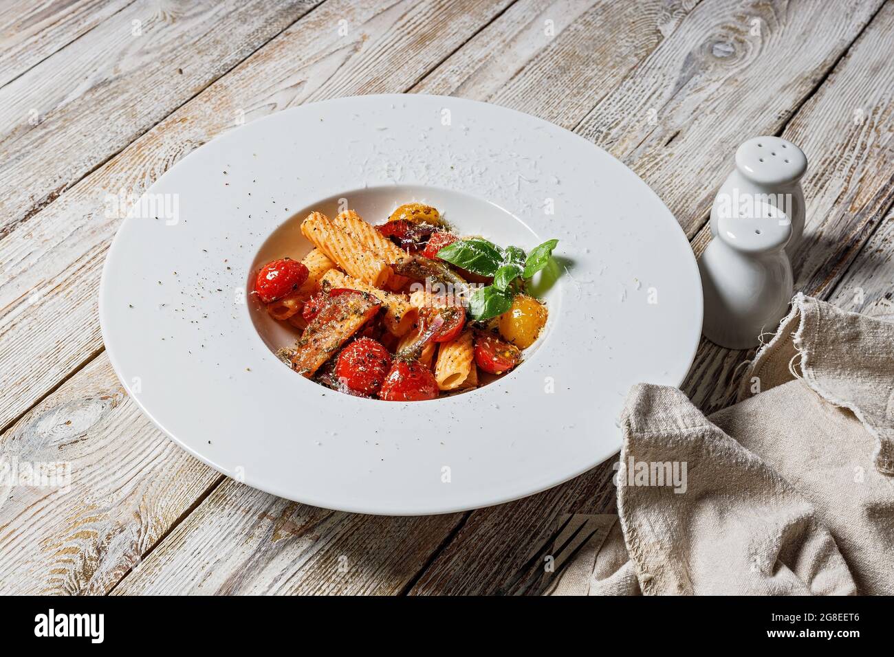 Close-up traditional penne pasta with tomatoes, spices, Parmesan cheese and fresh basil. Dish of classic Italian cuisine in a white plate on a wooden Stock Photo