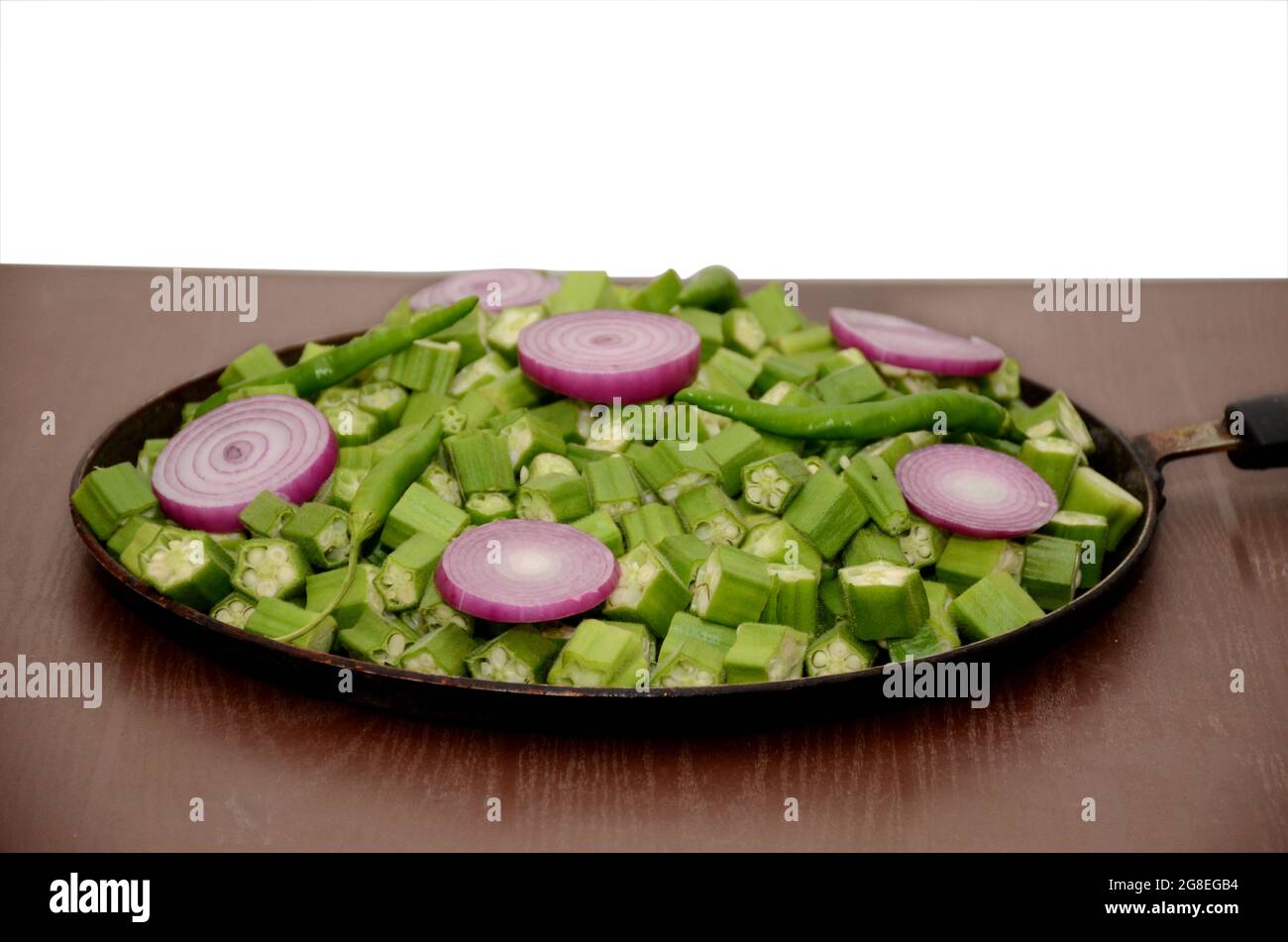 closeup the bunch ripe green sliced ladyfinger,onion,ripe green chilly in the fry pan isolated on white brown background. Stock Photo