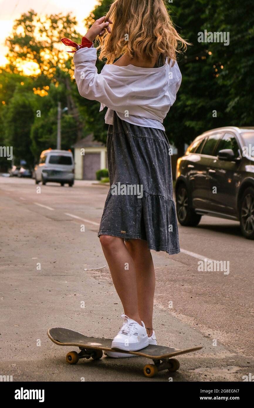 Millennial Woman in dress riding a skateboard on street. Skater girl on