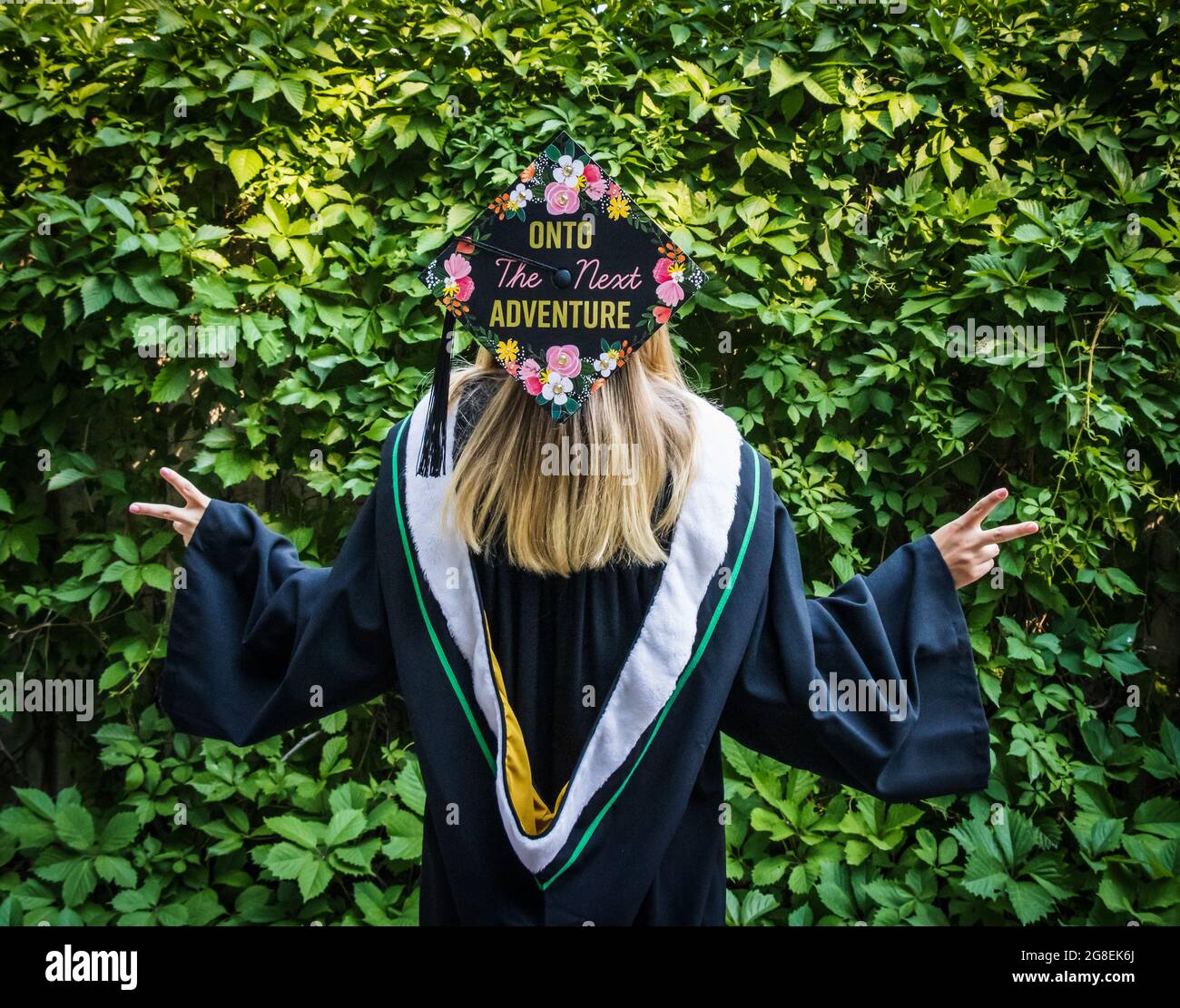 A humorous image of a woman in a convocation cap and gown with her head tilted backwards to show a message on the cap 'Onto the next adventure' Stock Photo