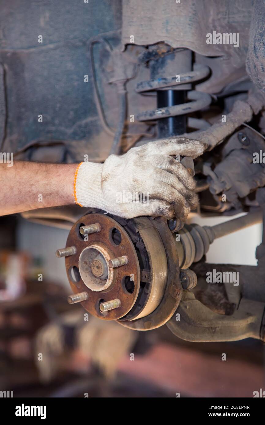 A man's gloved hand holds a rusty car wheel hub. In the garage, a man changes parts on a vehicle. Small business concept, car repair and maintenance service. UHD 4K. Stock Photo