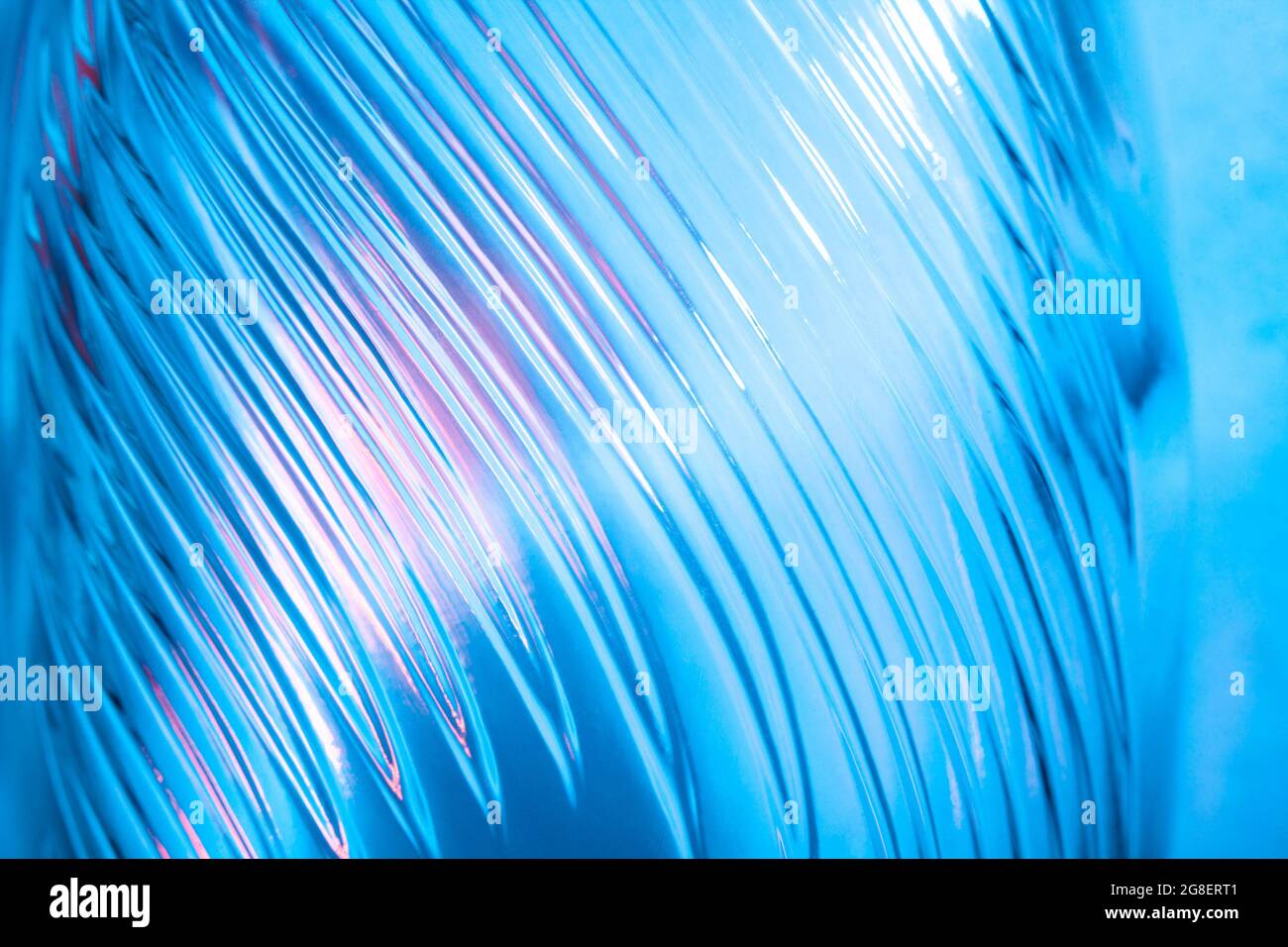 Abstract glass background. Texture of wavy glass illuminated with multi-colored light. Pink and blue stains. Close up. Flares on glass Stock Photo
