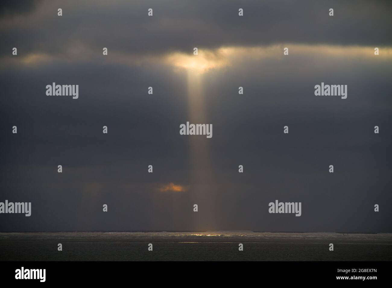 Sunrays from a dark and cloudy sky above a dark sea Stock Photo
