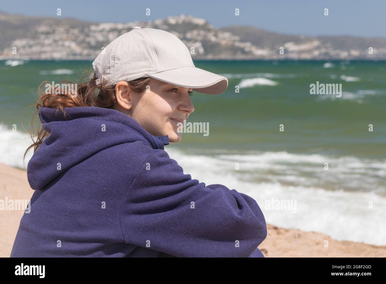 Natural portrait of a young caucasian woman, no retouching skin, no color correction. Girl outdoor portrait on a ocean background, brunette in basebal Stock Photo