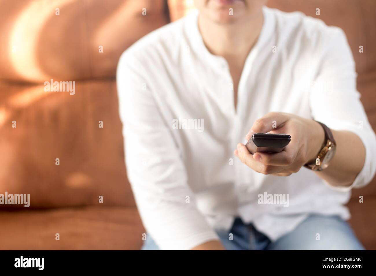 Young man sitting on sofa, holding remote control Stock Photo
