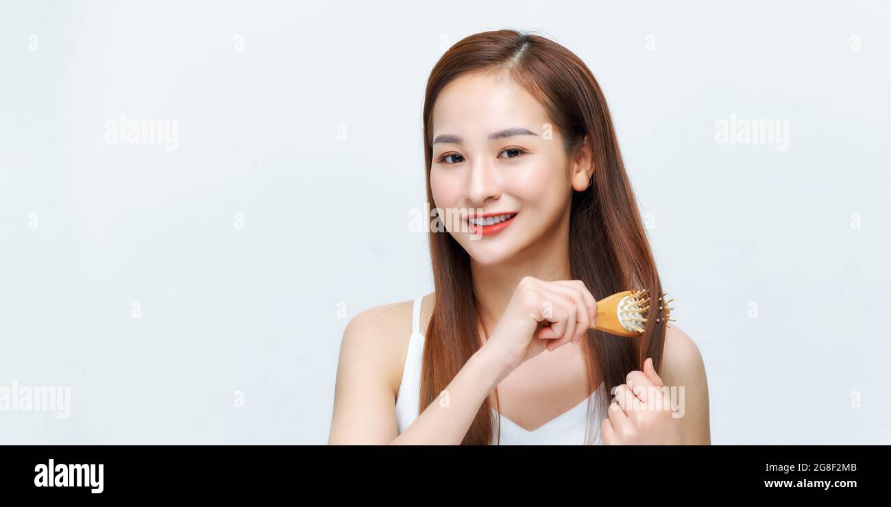 Portrait of beautiful young woman combing her hair, looking at camera and smiling Stock Photo