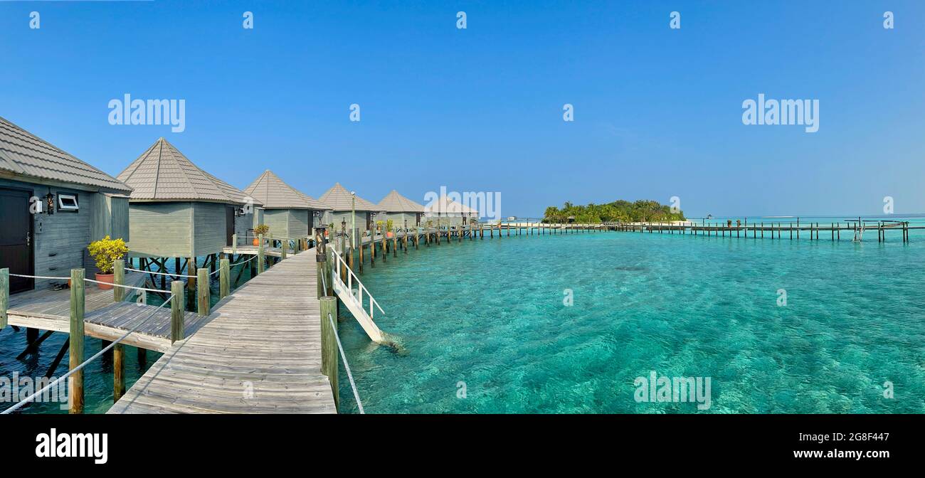 Panoramic View of Wooden Pier with Water Villa, Turquoise Ocean nad Island in Maldives. Maldivian Panorama of Overwater Bungalow and Laccadive Sea. Stock Photo