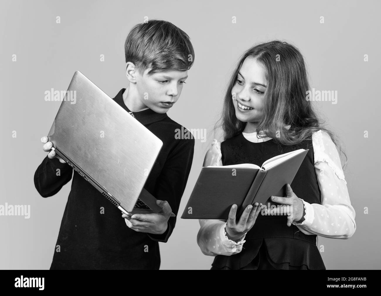 Digital technology for learning. Small children use new technology at school. Little girl and boy hold IT book and laptop. Technology in education Stock Photo