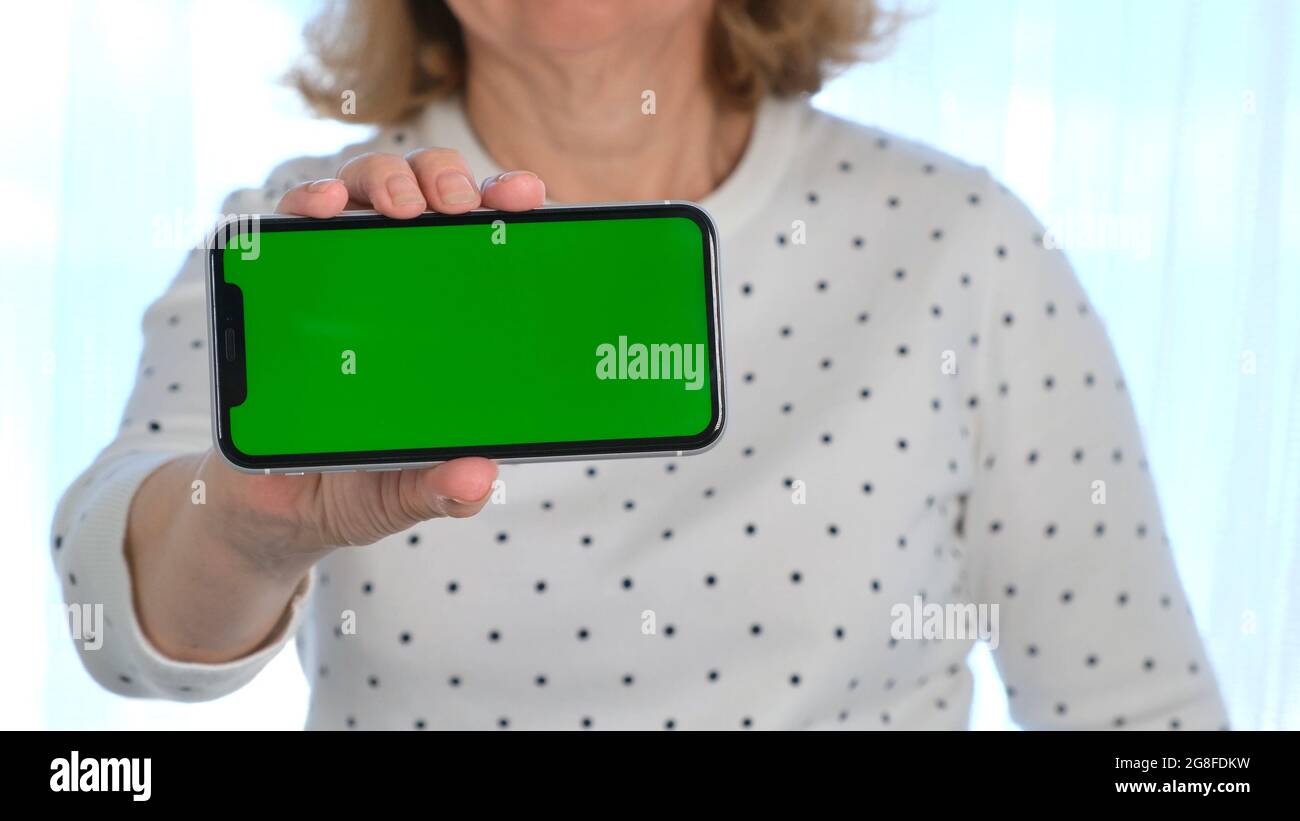 Middle-aged female senora uses an iPhone smartphone with a chroma key screen, copy space, close up. Online shopping concept, use of mobile Stock Photo
