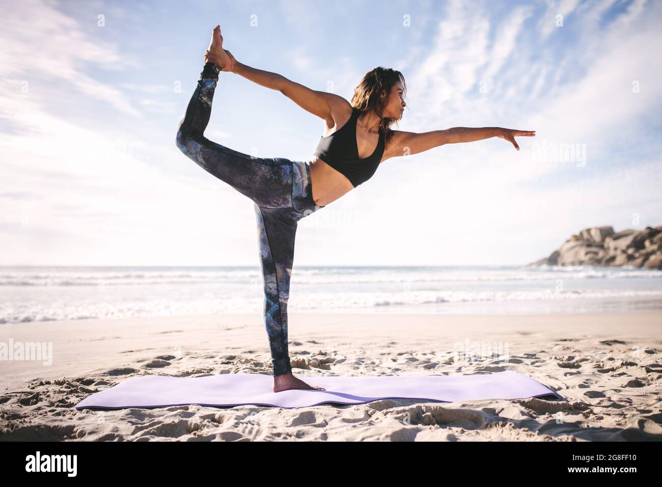 Side view of strong young woman standing on one leg holding foot at beach. Female doing