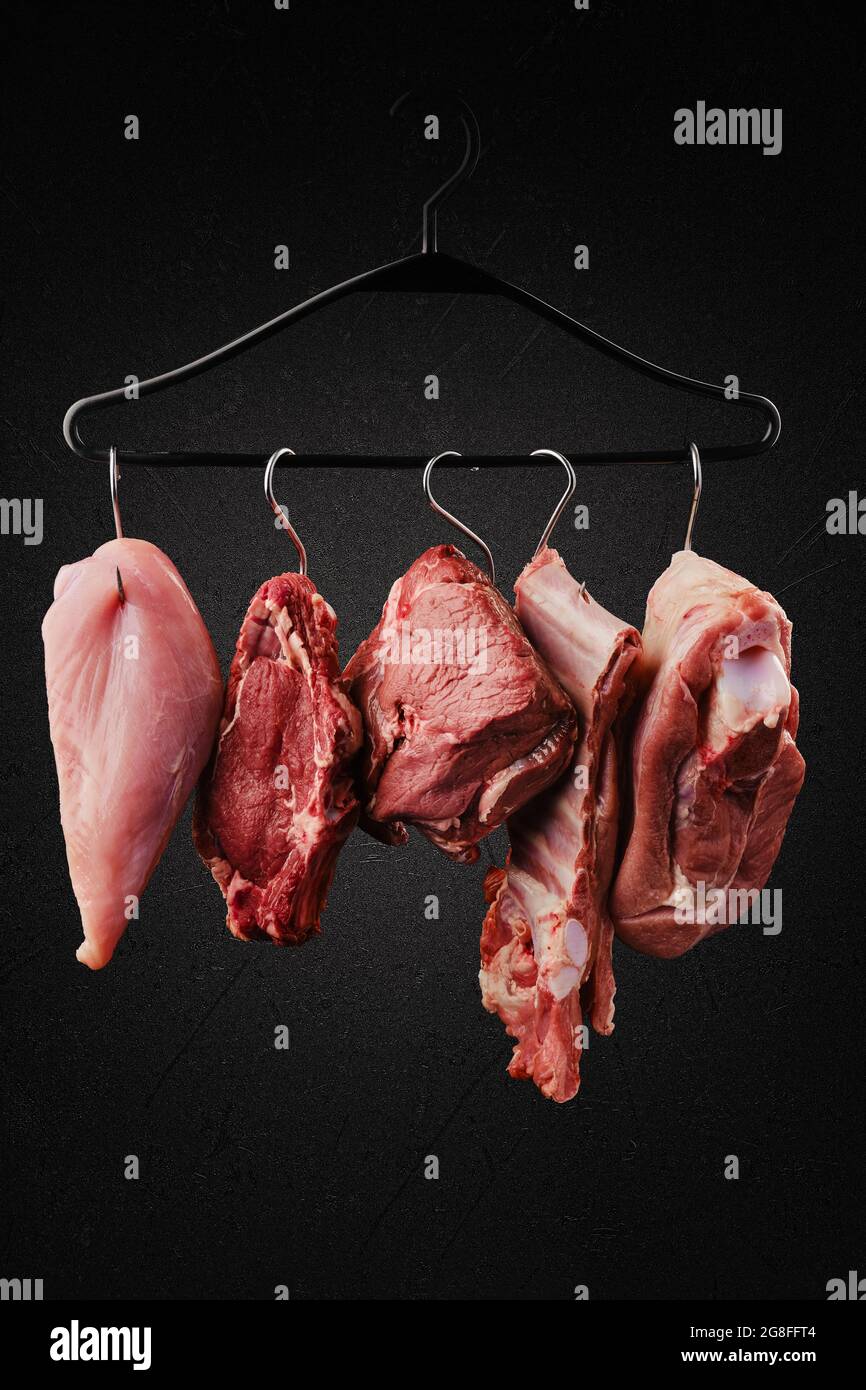 Different cuts of raw meat on hook on hanger over black background Stock Photo