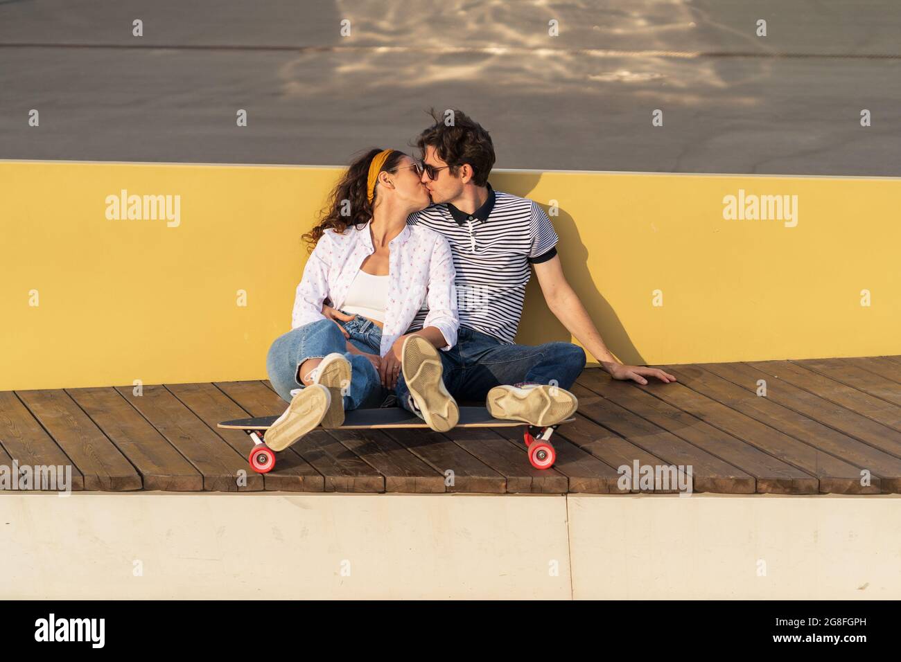 Trendy couple of skaters sit on longboard kissing. Romantic date of millennial hipsters outdoors Stock Photo