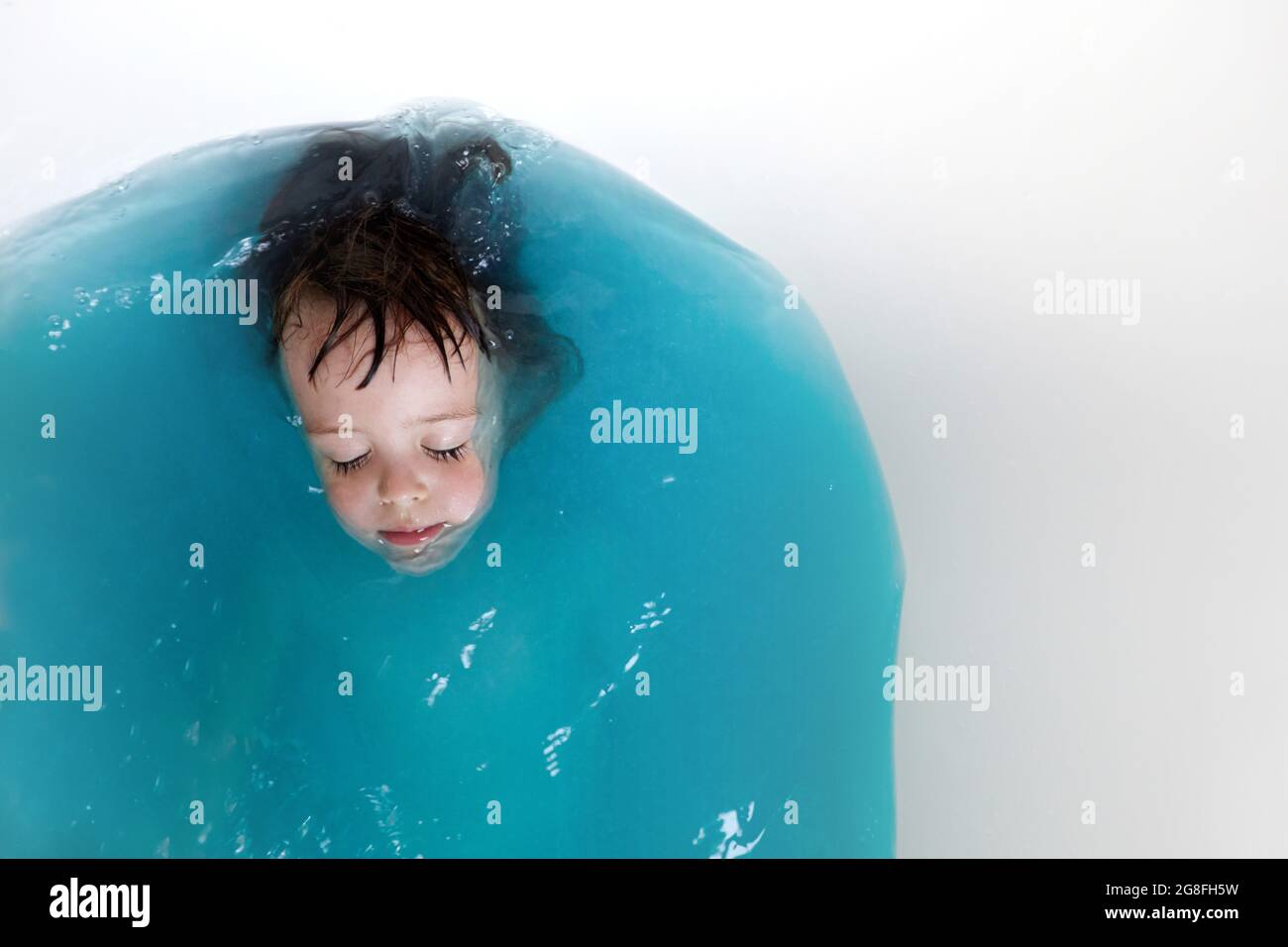 Top view of adorable little kid with closed eyes lying in bathtub with