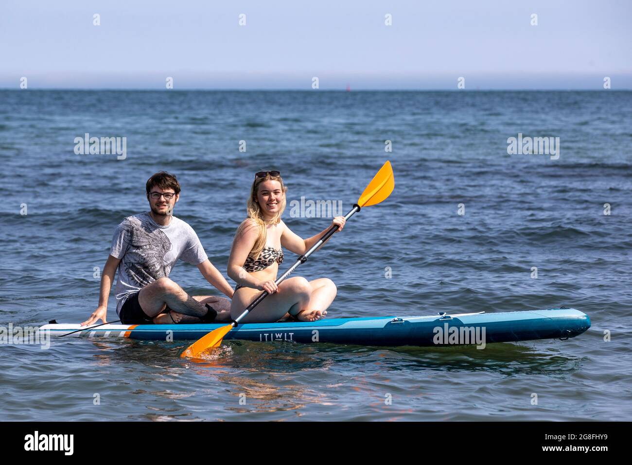 Aneurin Duffin-Murray (left) and Lauren Dalzell from Belfast on a paddle board at HelenÕs Bay beach in County Down, Northern Ireland. Picture date: Tuesday July 20 2021. Stock Photo