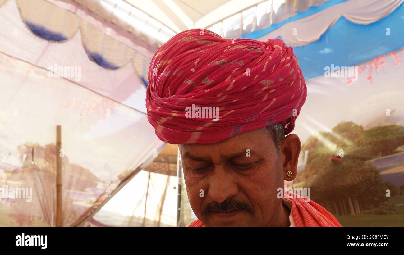 Closeup of a middle-aged South Asian man with an earring wearing a pagri inside a colorful tent Stock Photo
