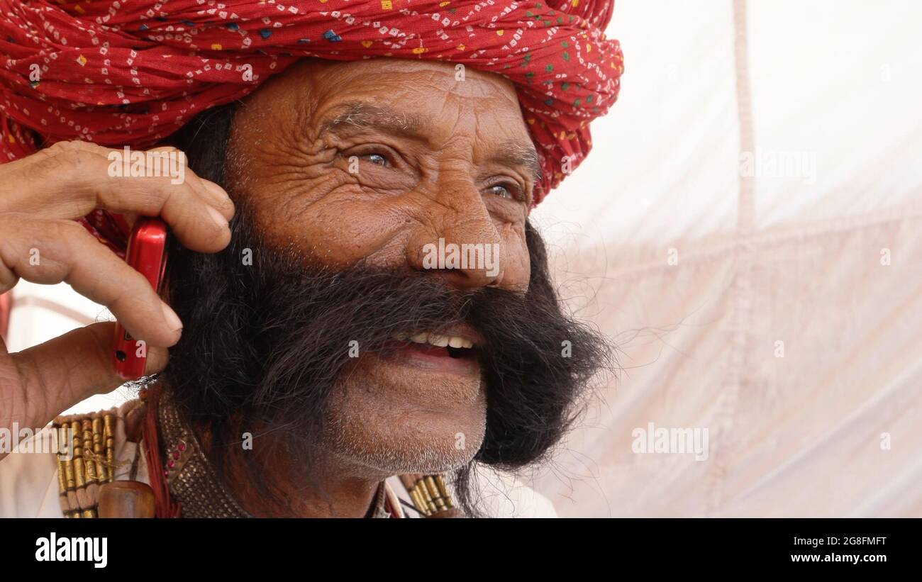 Closeup of an elderly South Asian man with a thick mustache and a pagri talking on the phone Stock Photo